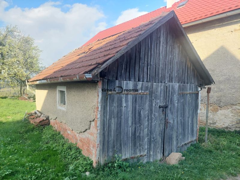 Eine alte Holzhütte auf einem Wohngrundstück in Budiná, umgeben von Grün und Bäumen.