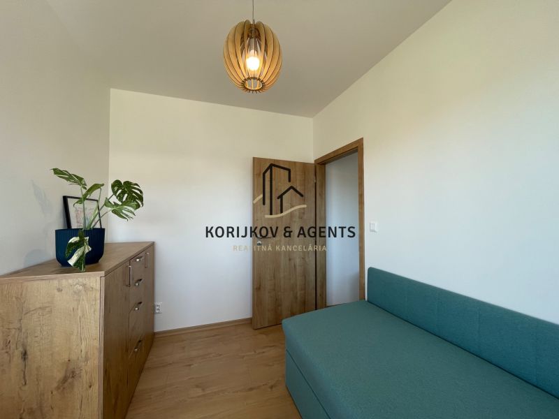 Ein Zimmer in einer 2-Zimmer-Wohnung mit einem Boden in Holzoptik und einem grünen Sofa.