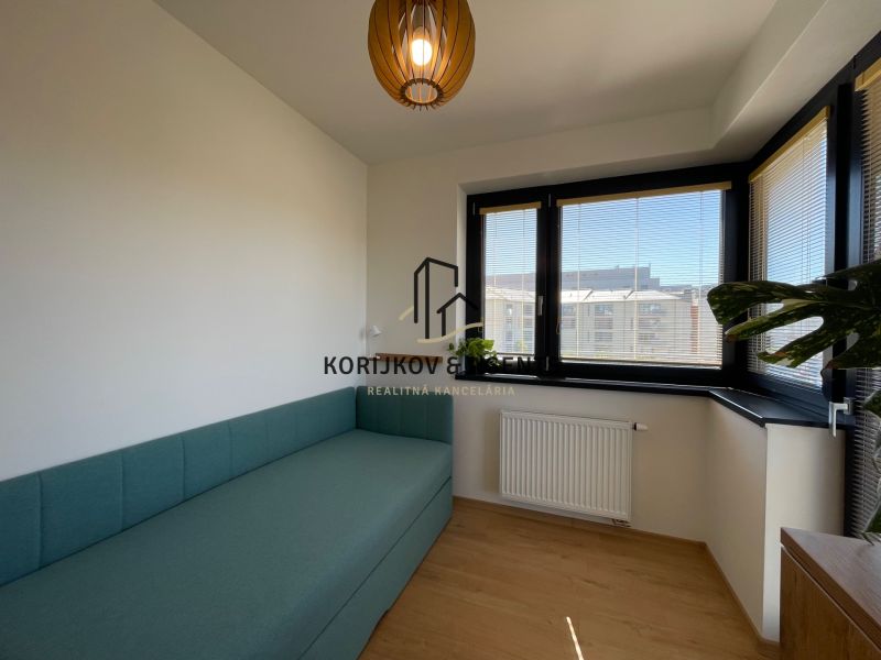 Ein Zimmer mit einem Sofa, Fenstern mit Jalousien und einem Holzboden in einer 2-Zimmer-Wohnung.