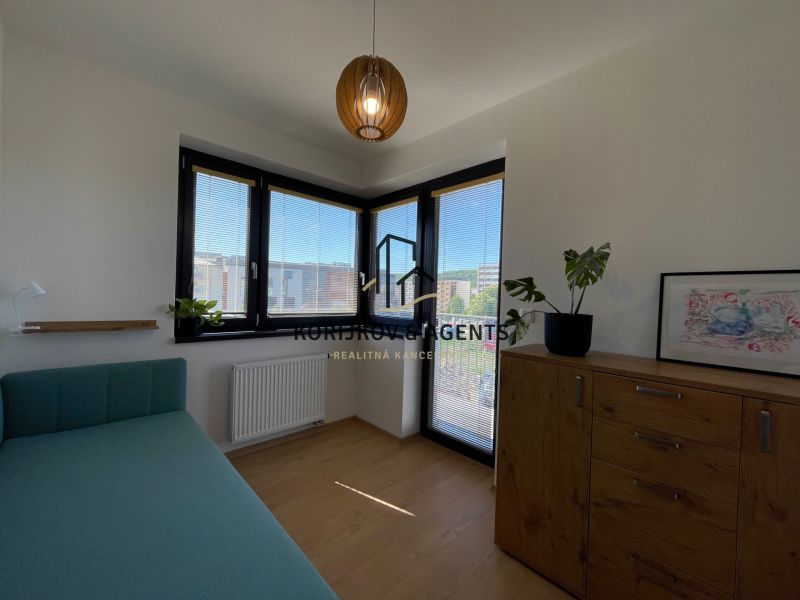 Ein Zimmer in einer 2-Zimmer-Wohnung mit einem Bett, einer Kommode und einem Boden in Holzoptik.