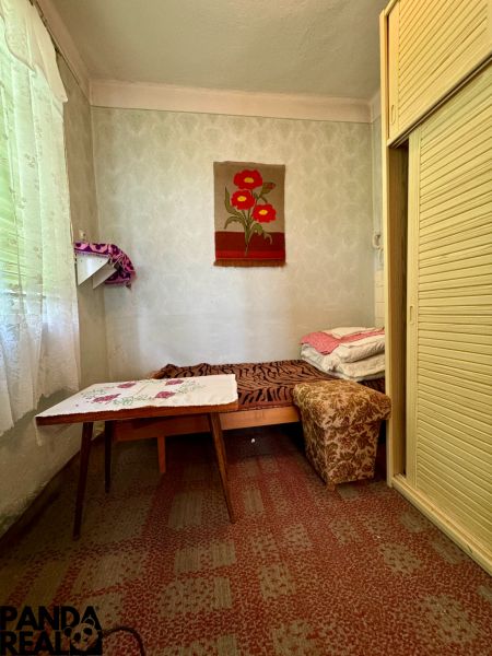 Ein Zimmer in einem Einfamilienhaus mit einem Bett, einem Tisch und einem Einbauschrank, dekorativer Teppich an der Wand.
