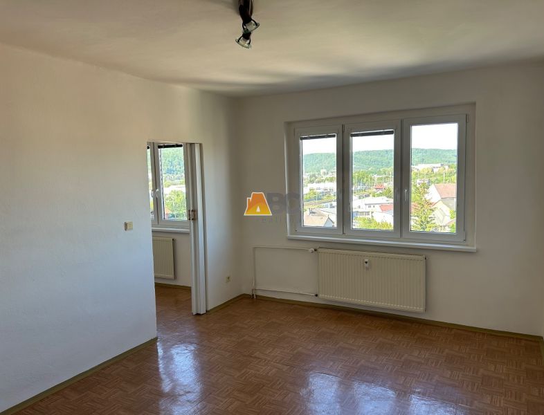 Helles Zimmer mit drei Fenstern und Holzboden in einer 2-Zimmer-Wohnung.