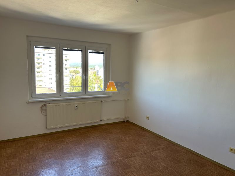 Ein Zimmer einer 2-Zimmer-Wohnung mit einem Boden in Holzoptik und einem großen Fenster.