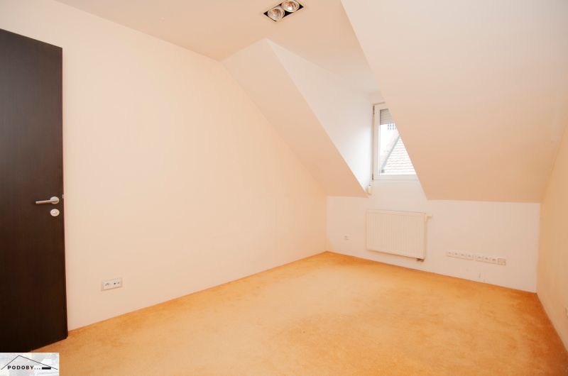 Ein leerer Raum mit einem bunten Teppich, einem Heizkörper und einem hellen Fenster in einer 3-Zimmer-Wohnung.