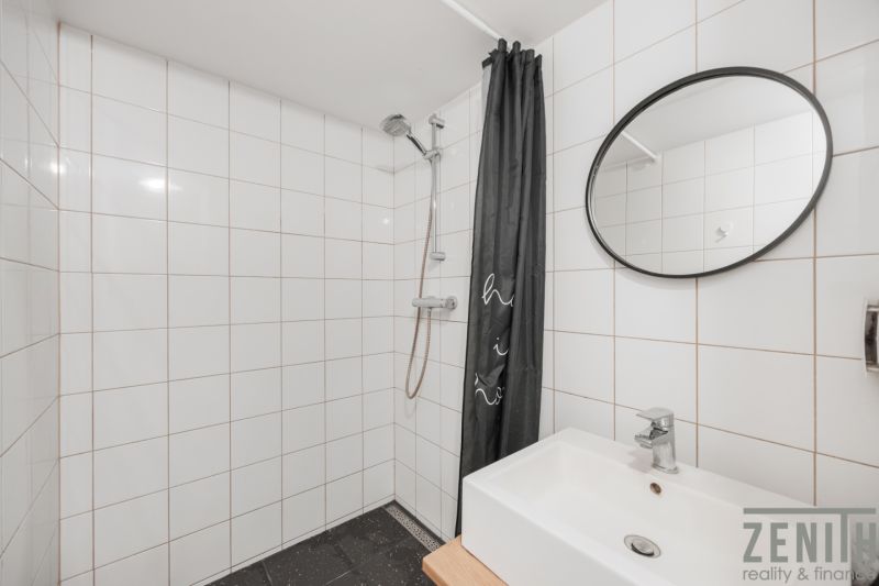 Badezimmer mit weißen Fliesen, Dusche und Waschbecken in einer 2-Zimmer-Wohnung.
