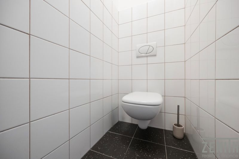 Toilette mit weißen Fliesen und schwarzem Boden in einer Zweizimmerwohnung.