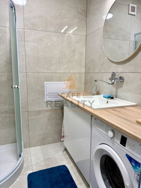 Badezimmer in einer Einzimmerwohnung mit Duschkabine, Waschmaschine und Spiegel über dem Waschbecken.