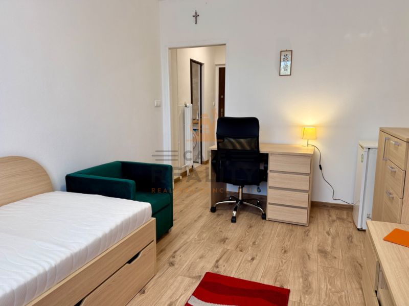Einzimmerwohnung mit Bett, Sessel, Schreibtisch und Holzboden.