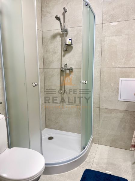 Duschkabine und Toilette im Badezimmer einer Einzimmerwohnung mit Fliesen.
