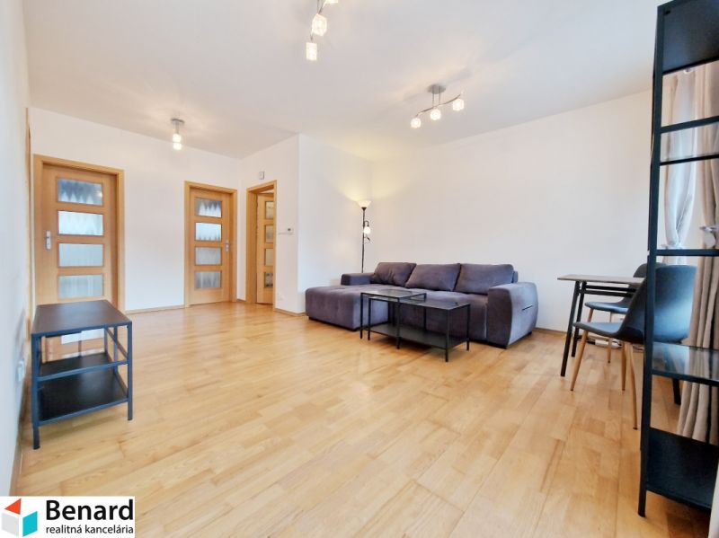 Ein Zimmer einer Dreizimmerwohnung mit einem Boden in Holzoptik, einem grauen Sofa und einem Tisch.