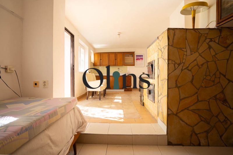 Ein Interieur in einem Einfamilienhaus mit Kamin, Bett, Küchenschränken und Tisch.