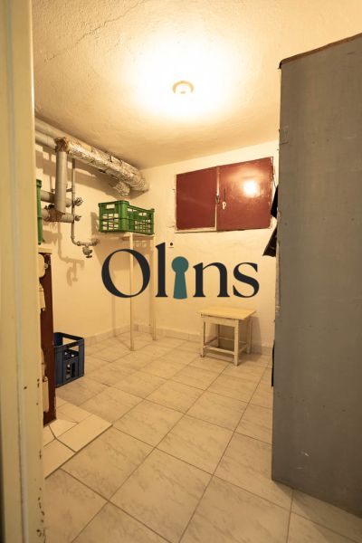 Praktischer Keller in einem Einfamilienhaus mit Fliesenboden, kleinen Möbeln und Rohrleitungen.