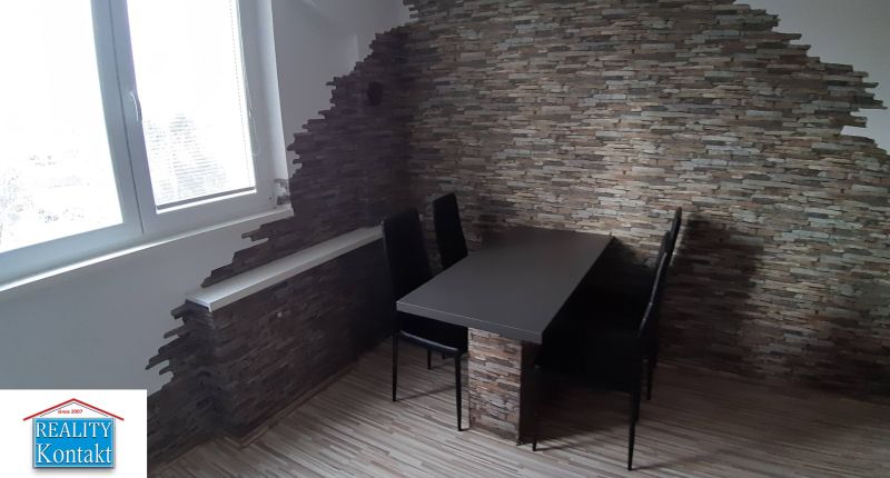 Essbereich mit Tisch und Stühlen in einer 2-Zimmer-Wohnung, Wand aus Stein.