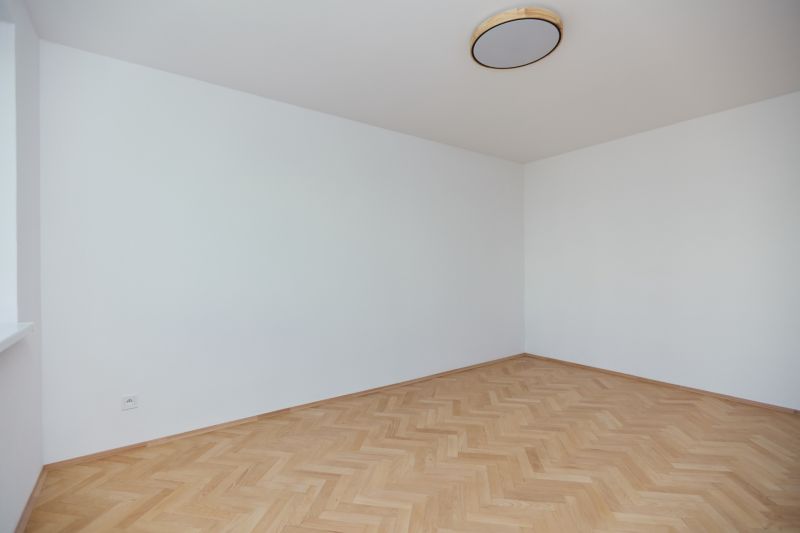 Ein leerer Raum mit weißen Wänden und einem Boden in Holzoptik in einer 3-Zimmer-Wohnung.