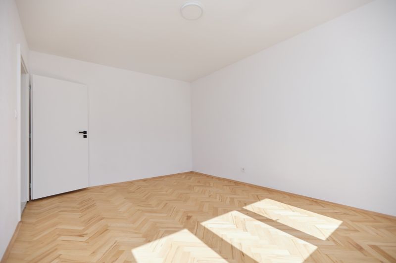 Ein leeres Zimmer in einer 3-Zimmer-Wohnung mit einem Boden in Holzoptik.