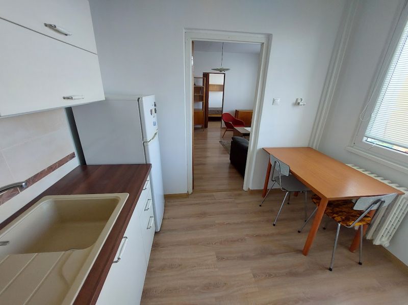 Küche in einer Einzimmerwohnung mit Esstisch und Boden in Holzoptik.