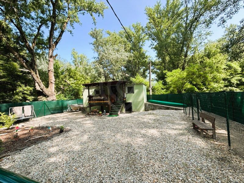 Eine Hütte in Gabčíkovo mit zwei Bänken im Hof, umgeben von Bäumen.