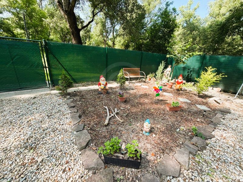 Ein Garten mit Zwergen und einer Bank bei der Hütte in Gabčíkovo, umgeben von Steinen und einem Zaun.
