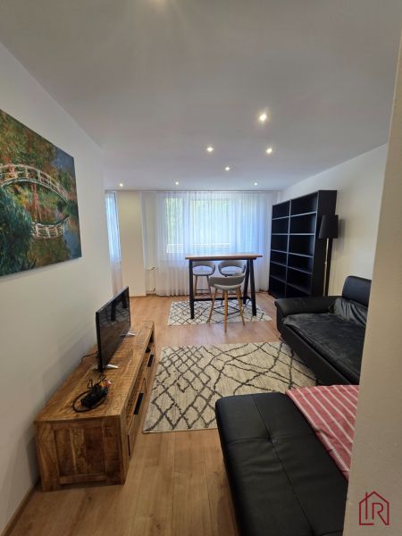 Wohnzimmer in einer 3-Zimmer-Wohnung mit schwarzem Sofa, Fernseher und Holzboden.