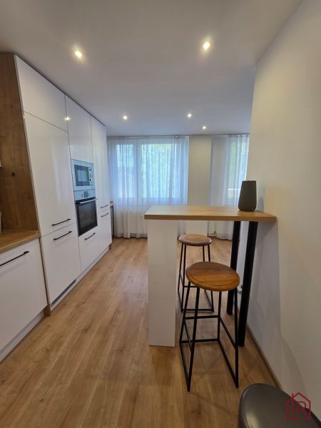 Küche mit weißen Schränken, Boden mit Holzdekor, hohe Stühle in einer 3-Zimmer-Wohnung.