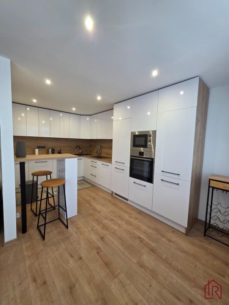Küche in einer 3-Zimmer-Wohnung mit Bar-Sitzgelegenheiten und einem Boden in Holzoptik.