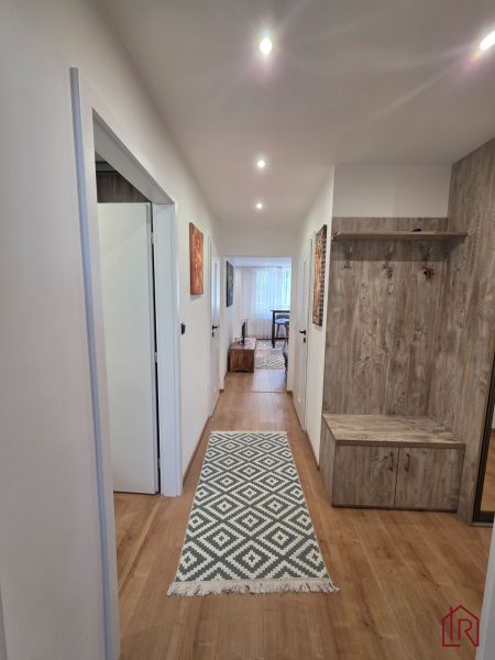 Flur in einer 3-Zimmer-Wohnung mit einem Boden in Holzoptik und einem Teppich mit geometrischem Muster.