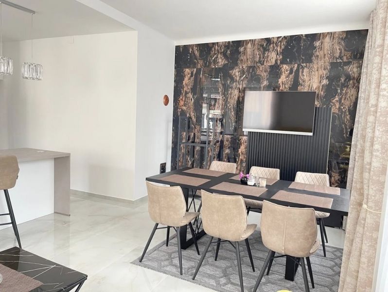 Esszimmer mit einem Tisch und sechs Stühlen, Holzboden, Fernseher an der Wand.