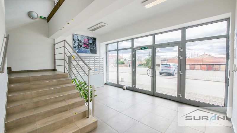 Innenraum eines Büros mit Treppe, Briefkästen und großen Glastüren.