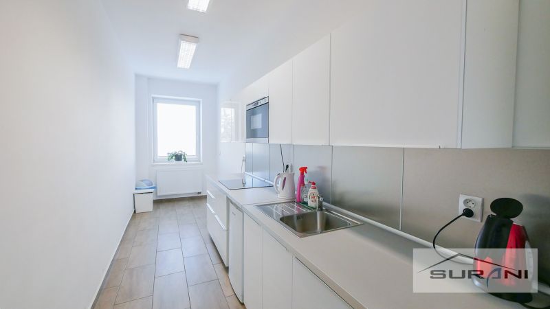 Büroküche mit hellen Möbeln und Geräten, mit einem Boden in Holzoptik.