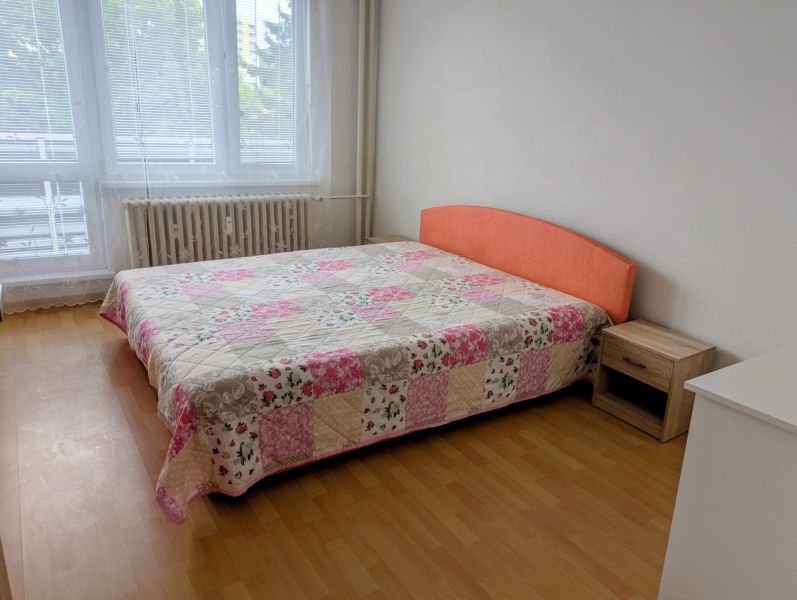 Schlafzimmer mit Bett und Patchwork-Überwurf in einer 2-Zimmer-Wohnung, Boden mit Holzdekor.