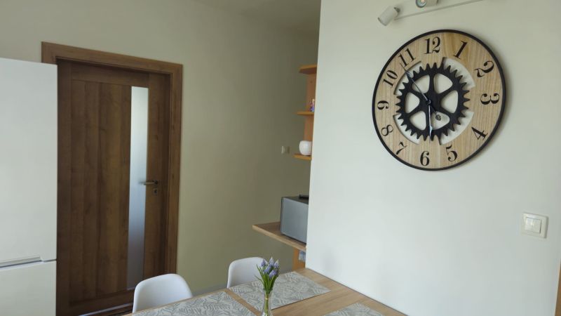 Interieur einer 2-Zimmer-Wohnung mit einer Uhr an der Wand, Holztüren und einem Tisch.