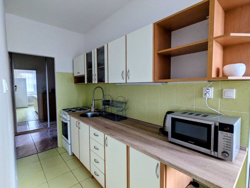 Küche in einer 2-Zimmer-Wohnung mit Mikrowelle und Kochfeld, die in einen weiteren Raum führt.
