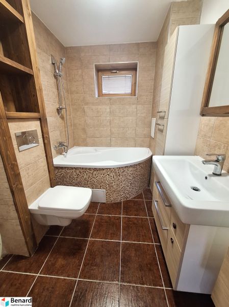 Badezimmer in einer 2-Zimmer-Wohnung mit Badewanne und Schränken, hellbraune Fliesen und Bodenfliesen.