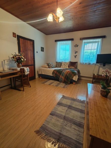 Ein Zimmer mit einem Sofa, einem Holzboden, Blumen und einem Tisch in einem Einfamilienhaus.