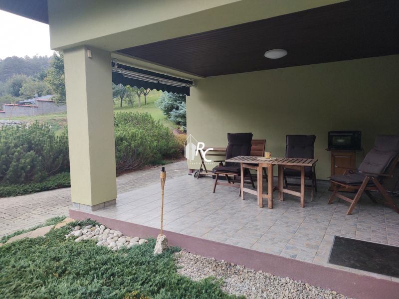 Die Terrasse des Einfamilienhauses in Trebostovo mit Holzgartenmöbeln und gepflegtem Grün.