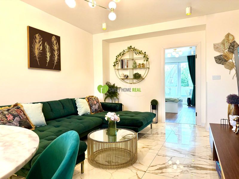 Innenraum einer 3-Zimmer-Wohnung mit Sofa, Glastisch und künstlerischen Dekorationen an der Wand.