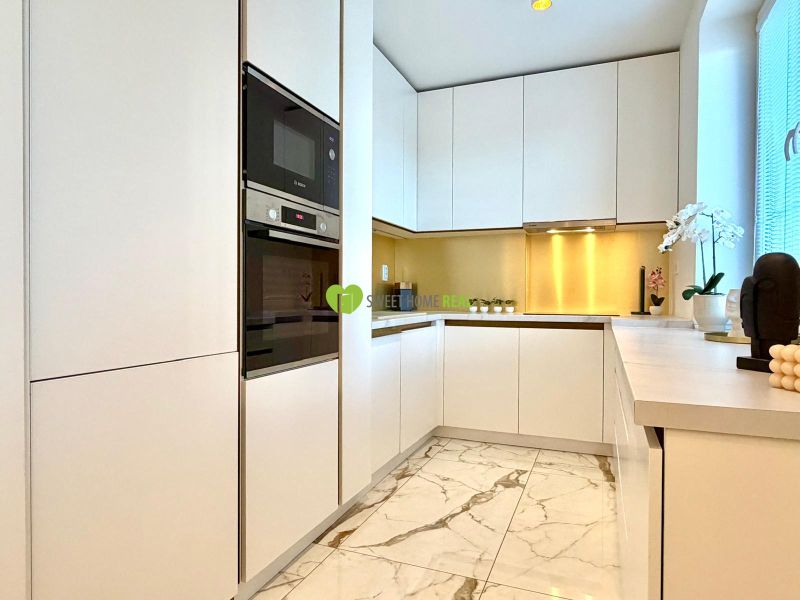 Weiße Küche in einer 3-Zimmer-Wohnung mit Marmorboden und eingebauten Geräten.