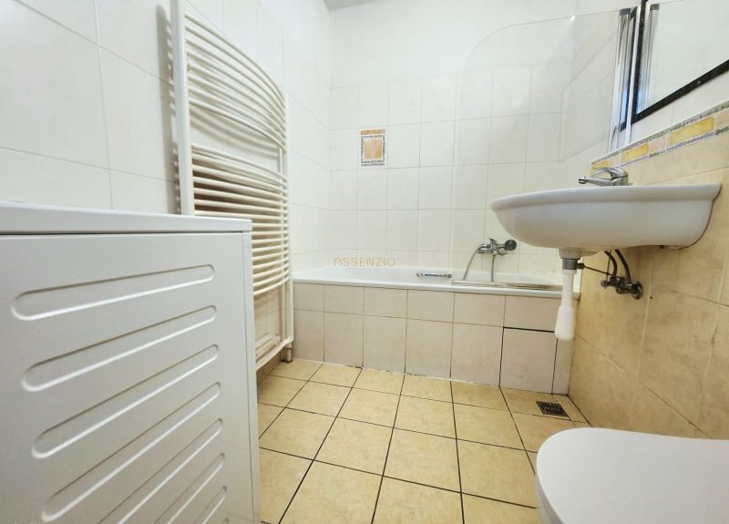 Badezimmer in einer 2-Zimmer-Wohnung mit Badewanne, Waschbecken und Waschmaschine, gefliest mit weißen Fliesen.