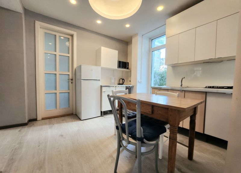Küche in einer 2-Zimmer-Wohnung mit Holzboden, weißer Küchenzeile und Fenster.