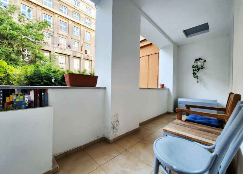 Ein Balkon in einer 2-Zimmer-Wohnung mit Blumentöpfen und Holzmöbeln.