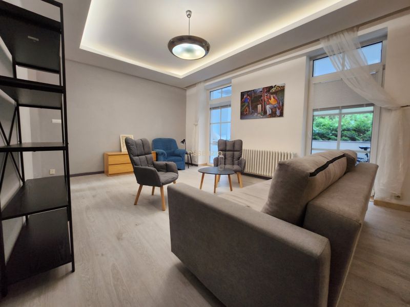 Wohnzimmer mit grauem Sofa, Holzboden und Sesseln in einer Zweizimmerwohnung.