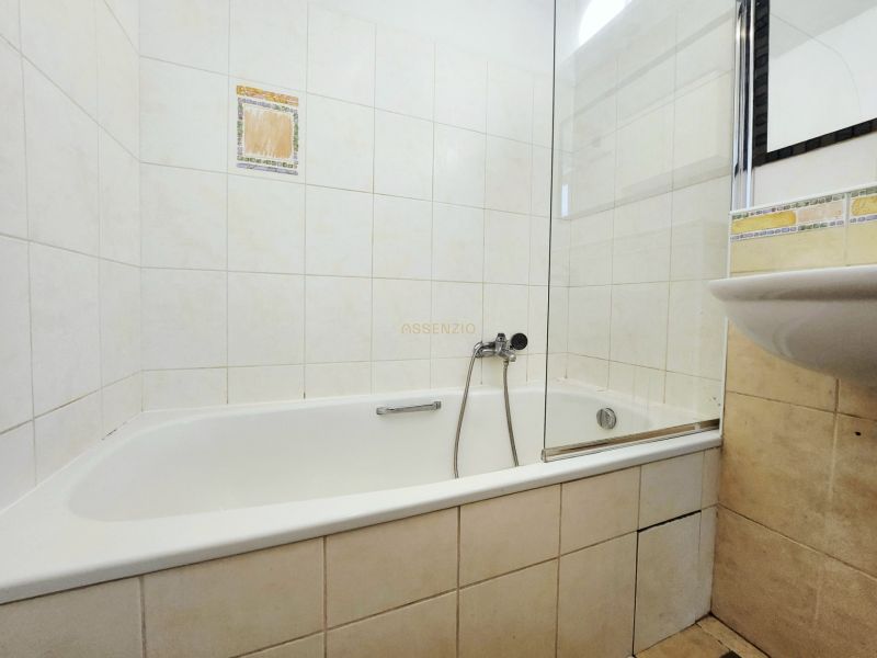 Badezimmer in einer 2-Zimmer-Wohnung mit Badewanne und Waschbecken, gefliest mit hellen Fliesen.
