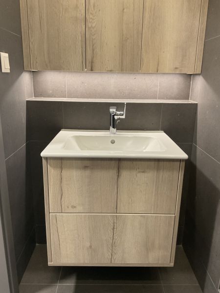 Kompaktes Badezimmer mit Schrank und Waschbecken in einer Einzimmerwohnung, helles Holz und dunkle Fliesen.