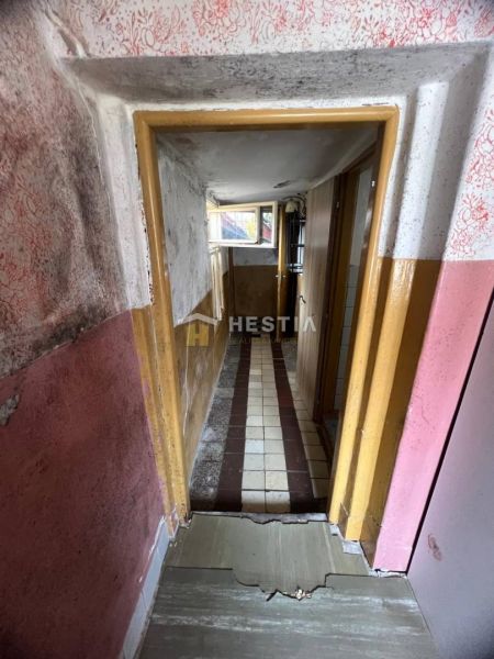 Ein enger Flur mit beschädigten Wänden und einem gefliesten Boden in einem Einfamilienhaus.
