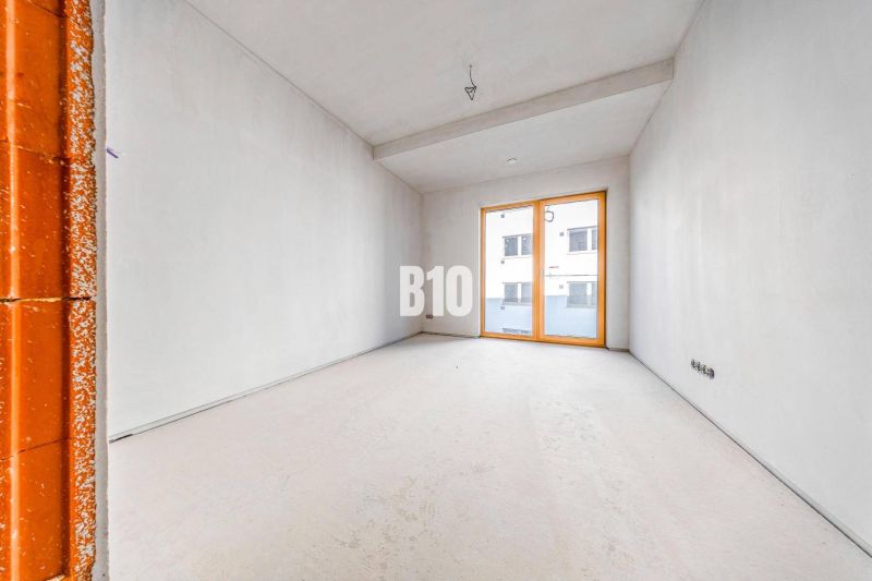 Ein leerer Raum mit Betonboden und großen Fenstern in einer 3-Zimmer-Wohnung.