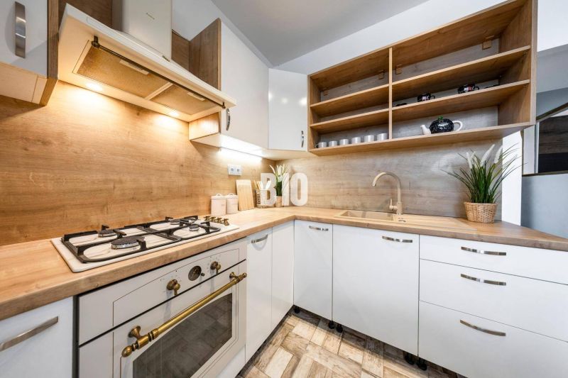 Küche in einer 2-Zimmer-Wohnung, helle Schränke, offene Regale, Boden mit Holzdekor.