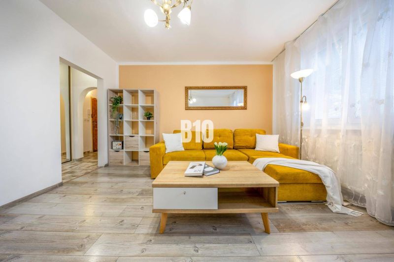 Wohnzimmer in einer 2-Zimmer-Wohnung mit gelbem Sofa und Holzboden.