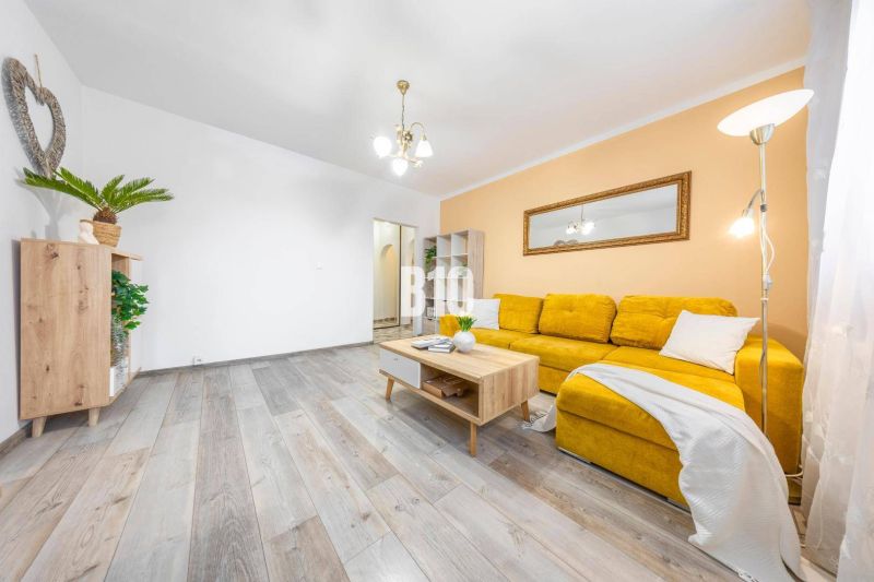 Wohnzimmer in einer 2-Zimmer-Wohnung mit Holzboden und gelbem Sofa.