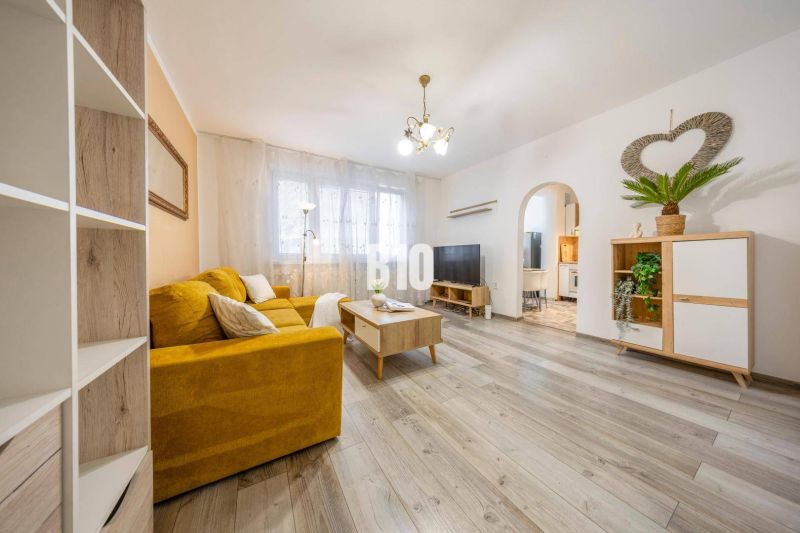 Wohnzimmer in einer Zweizimmerwohnung mit gelbem Sofa und Holzboden.