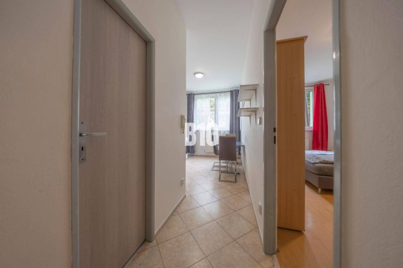 Eingangsflur zum Büro mit Fliesenboden und Blick in den Raum mit Fenstern.